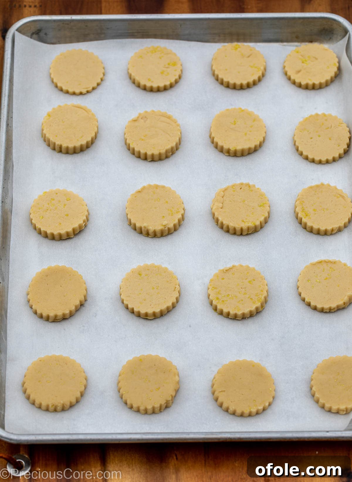 Neatly arranged cut-out lemon shortbread cookie dough rounds on a baking sheet lined with parchment paper.