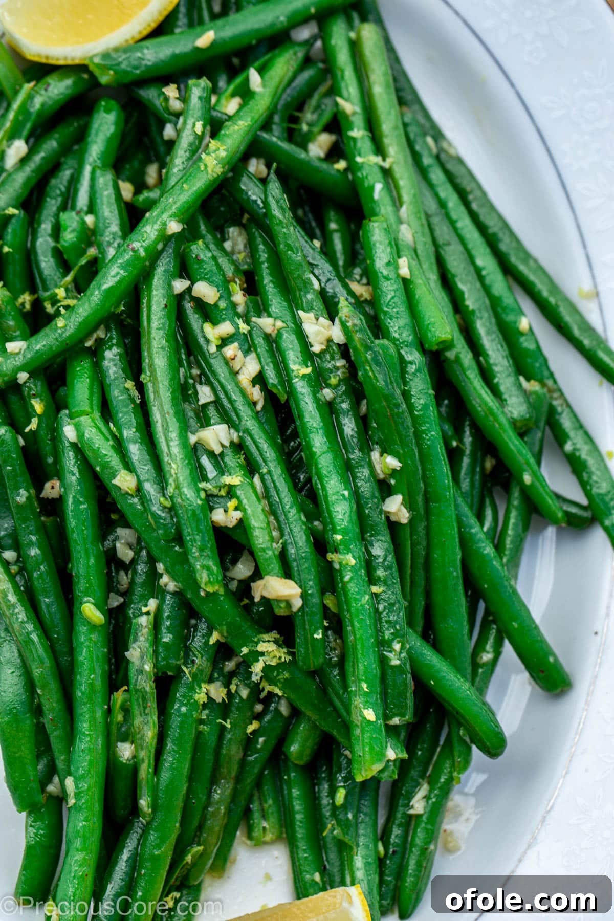 Cooked garlic butter green beans on a white serving tray, garnished with fresh herbs.