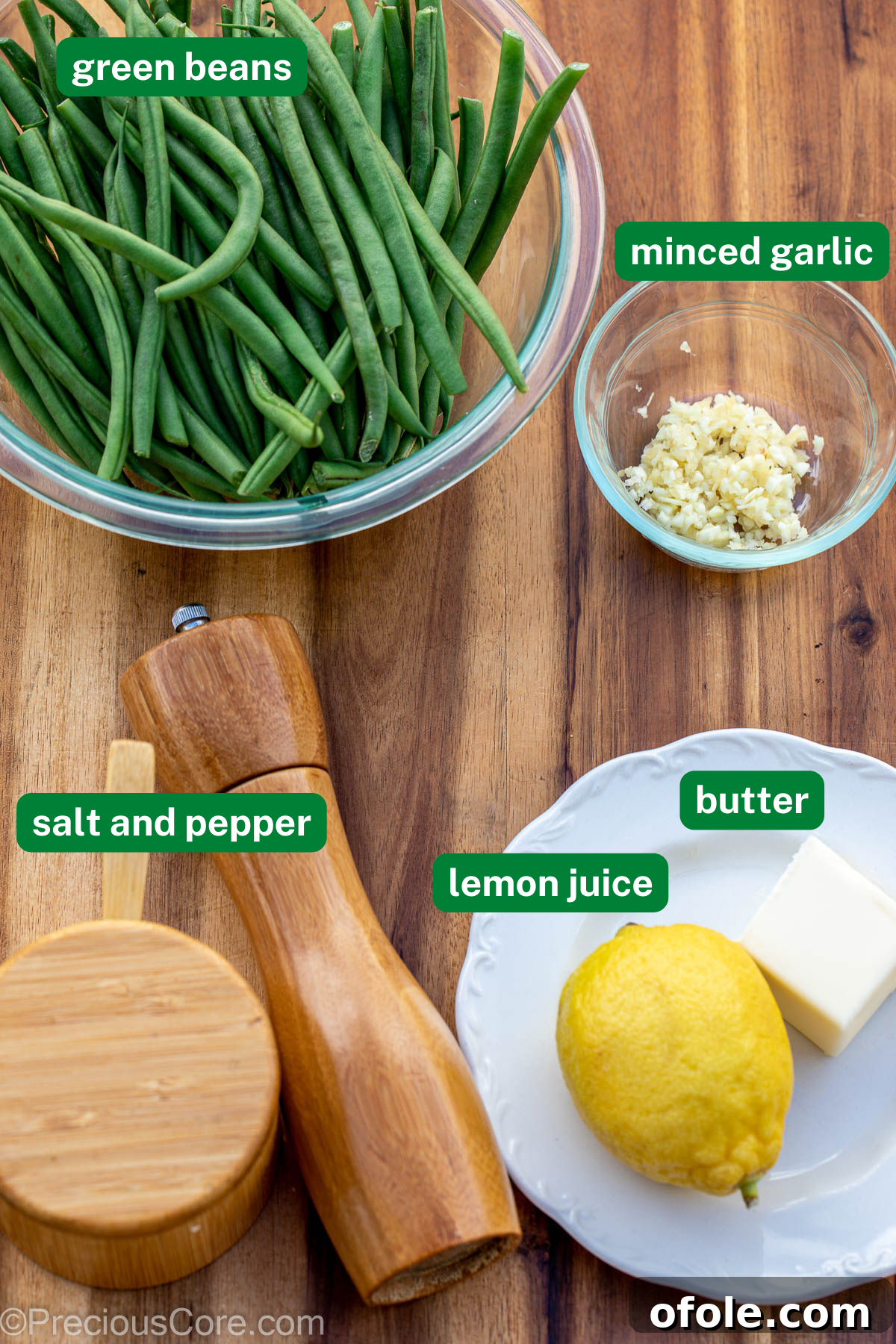 Fresh green beans, minced garlic, salt and pepper, lemon, and butter laid out on a chopping board.