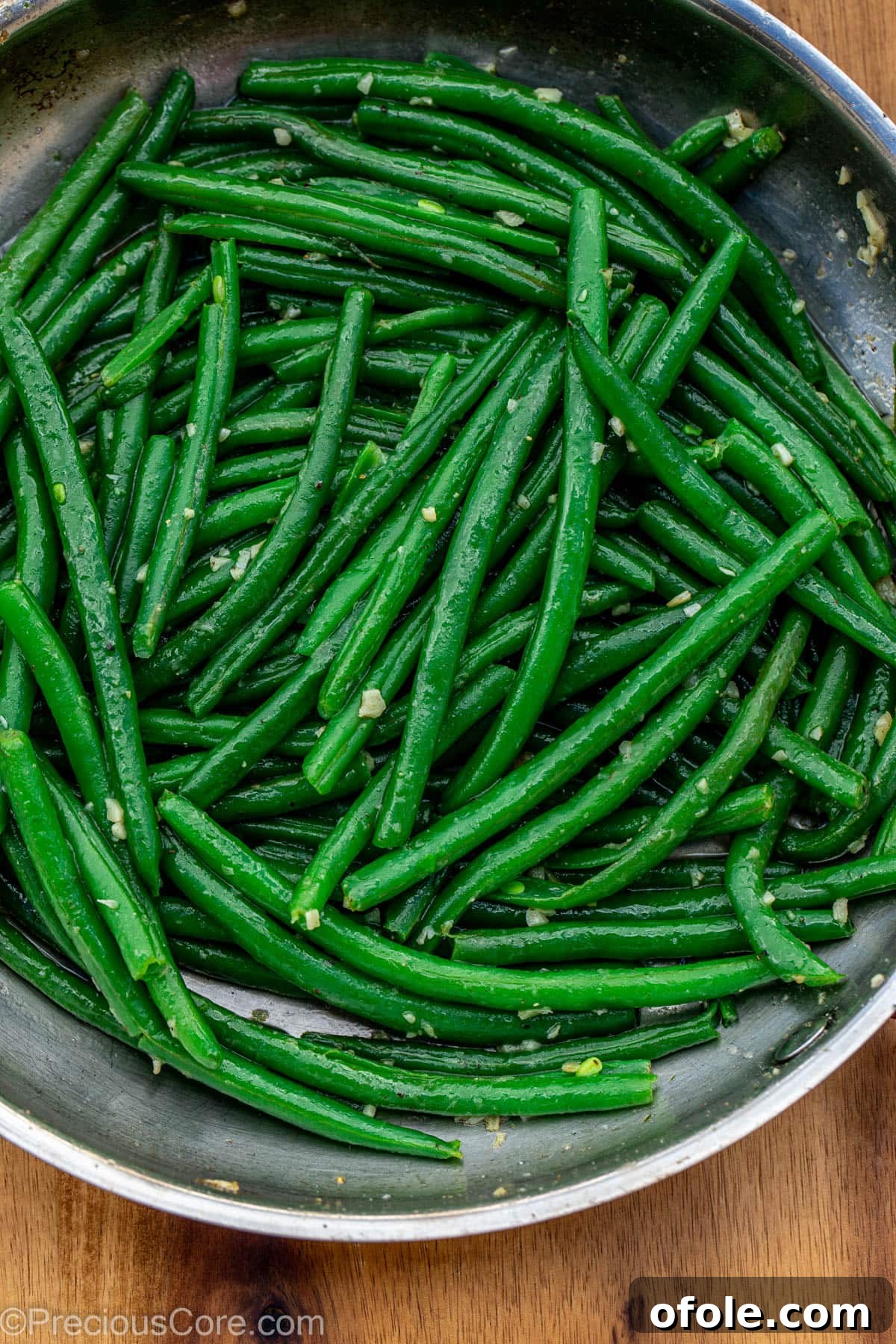 Green beans added to the skillet with garlic and butter, being tossed to combine.