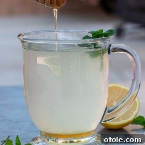 Honey dipper dripping honey into a cup of honey lemon tea.