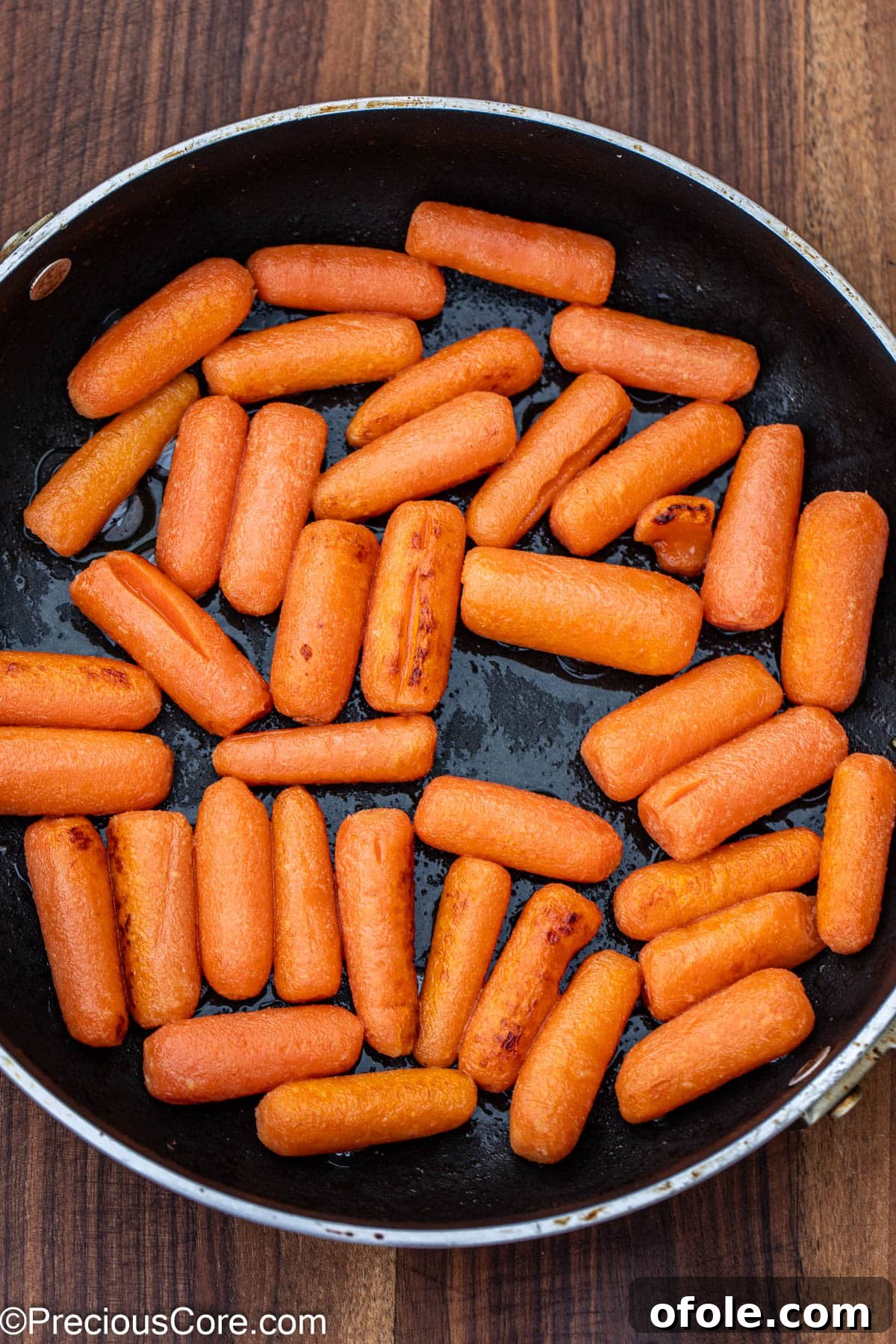 Carrots cooking in butter in a skillet, starting to get a golden-brown hue.