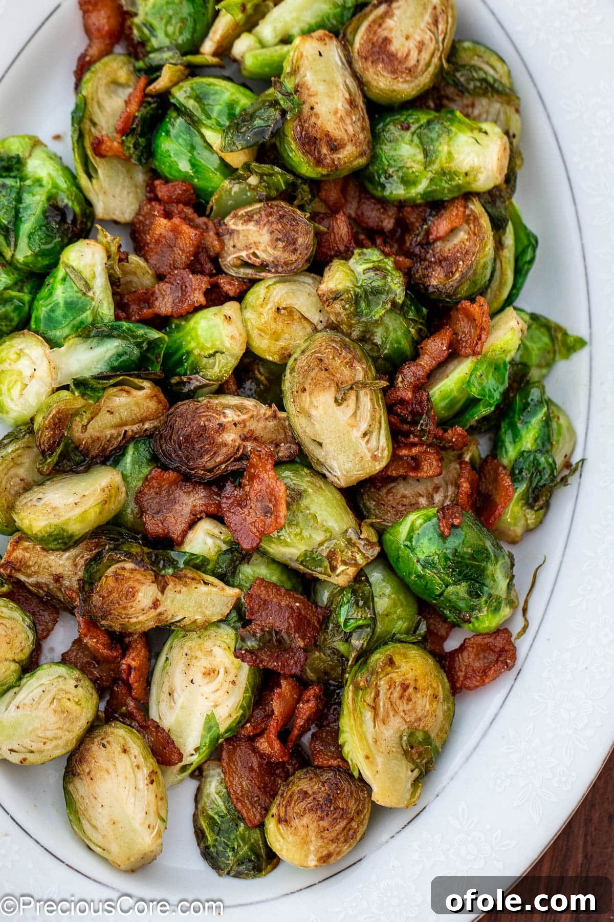 Cooked bacon and Brussels sprouts artfully arranged on a pristine white serving plate.