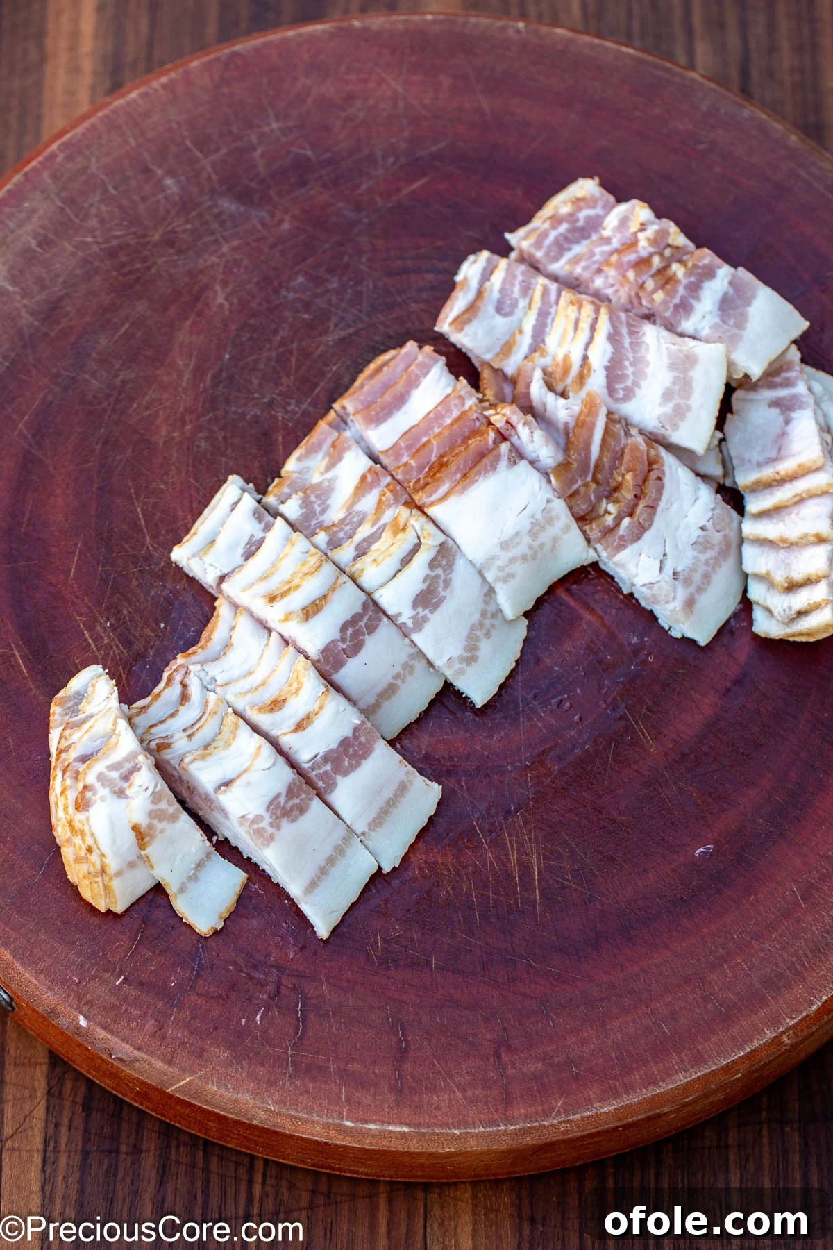 Sliced bacon on a round chopping board, ready for cooking.