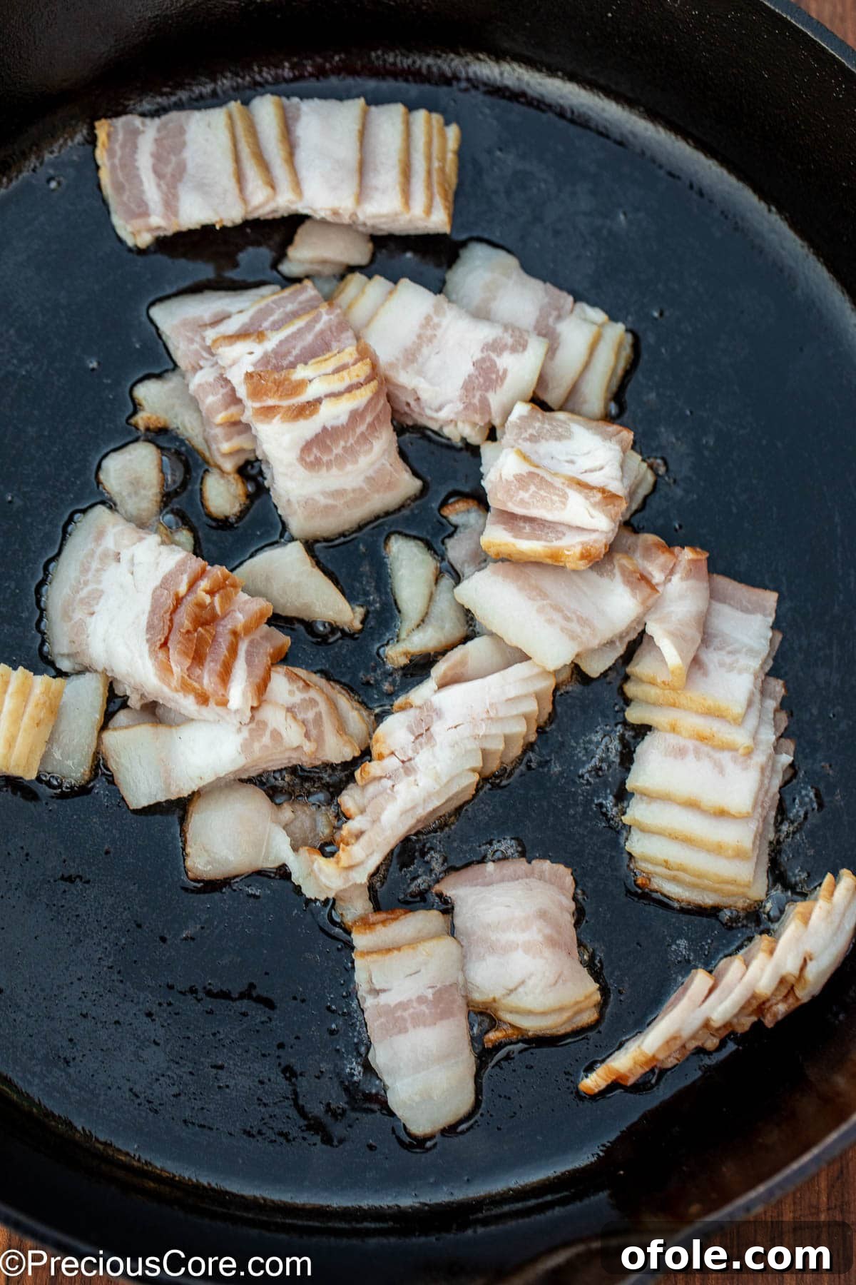 Sliced bacon frying in a cast iron skillet, rendering its fat.