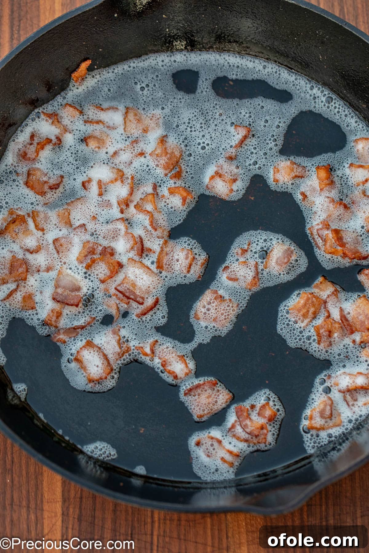 Browned and crispy bacon bits in rendered bacon grease, glistening in a skillet.