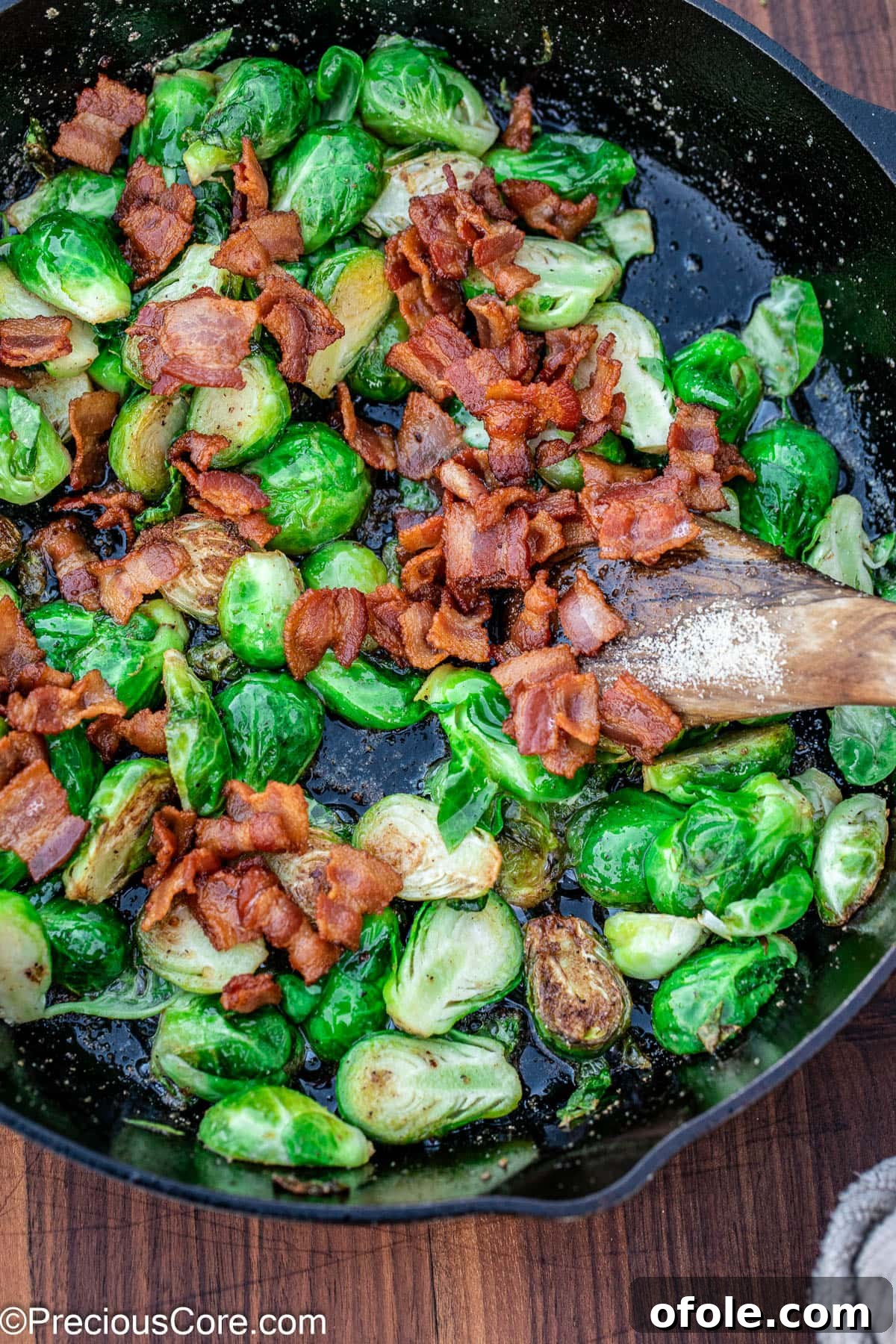 Pan fried Brussels sprouts, golden and tender, in a skillet with the crispy bacon just added back.