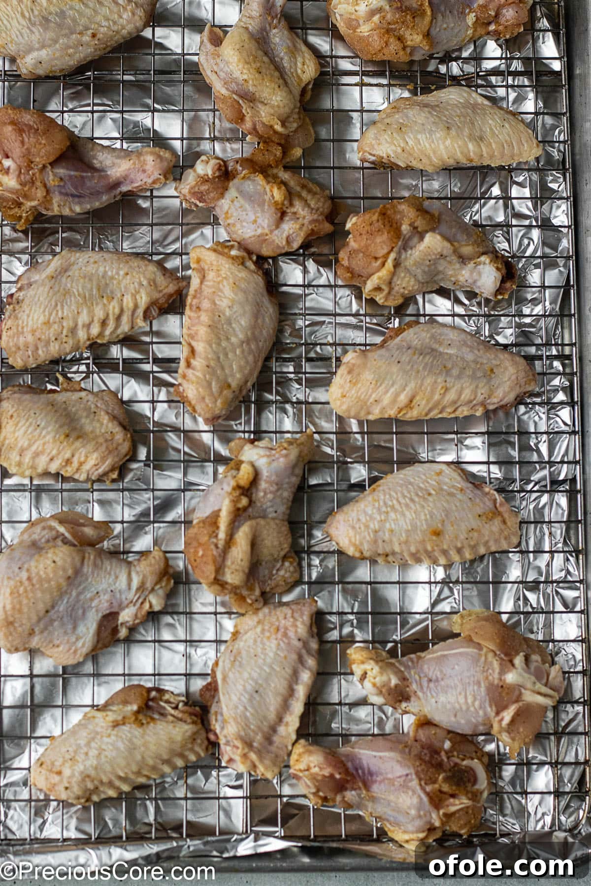 Garlic Gold Wings 6 Raw chicken wings meticulously arranged on a wire rack, which is placed on a baking sheet, ready for the oven.