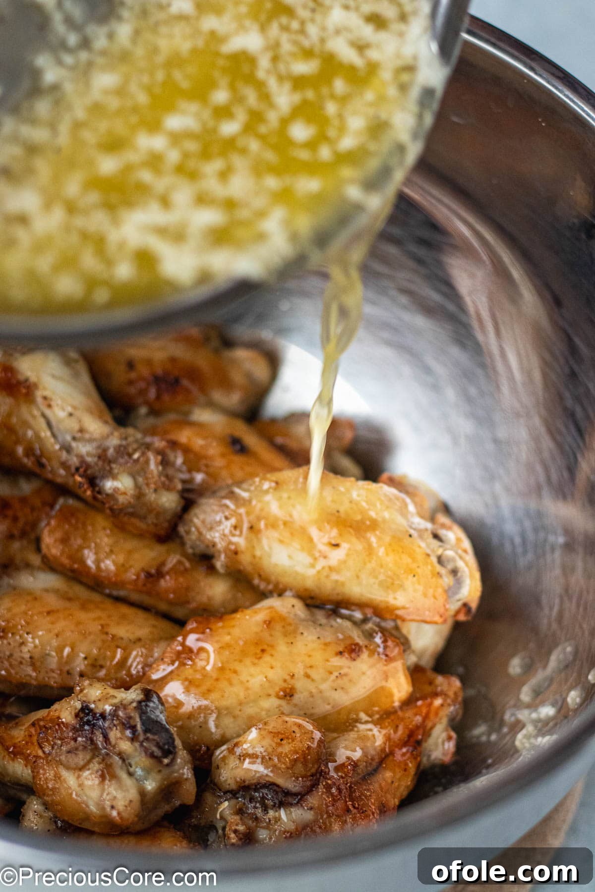 Garlic Gold Wings 9 A stream of rich garlic butter sauce being poured over a bowl of cooked chicken wings, ready to be tossed.
