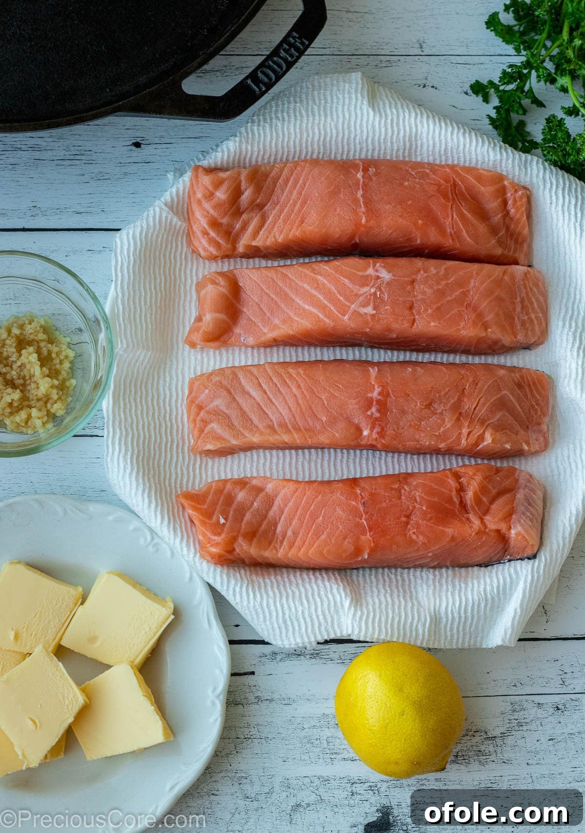 Key ingredients for lemon butter salmon: raw salmon fillets, minced garlic, butter, and fresh lemons, arranged on a wooden board.
