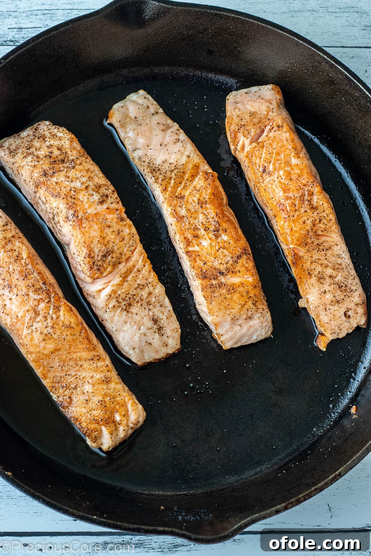 Perfectly seared salmon fillets, skin-side down, cooking in a hot cast iron skillet.