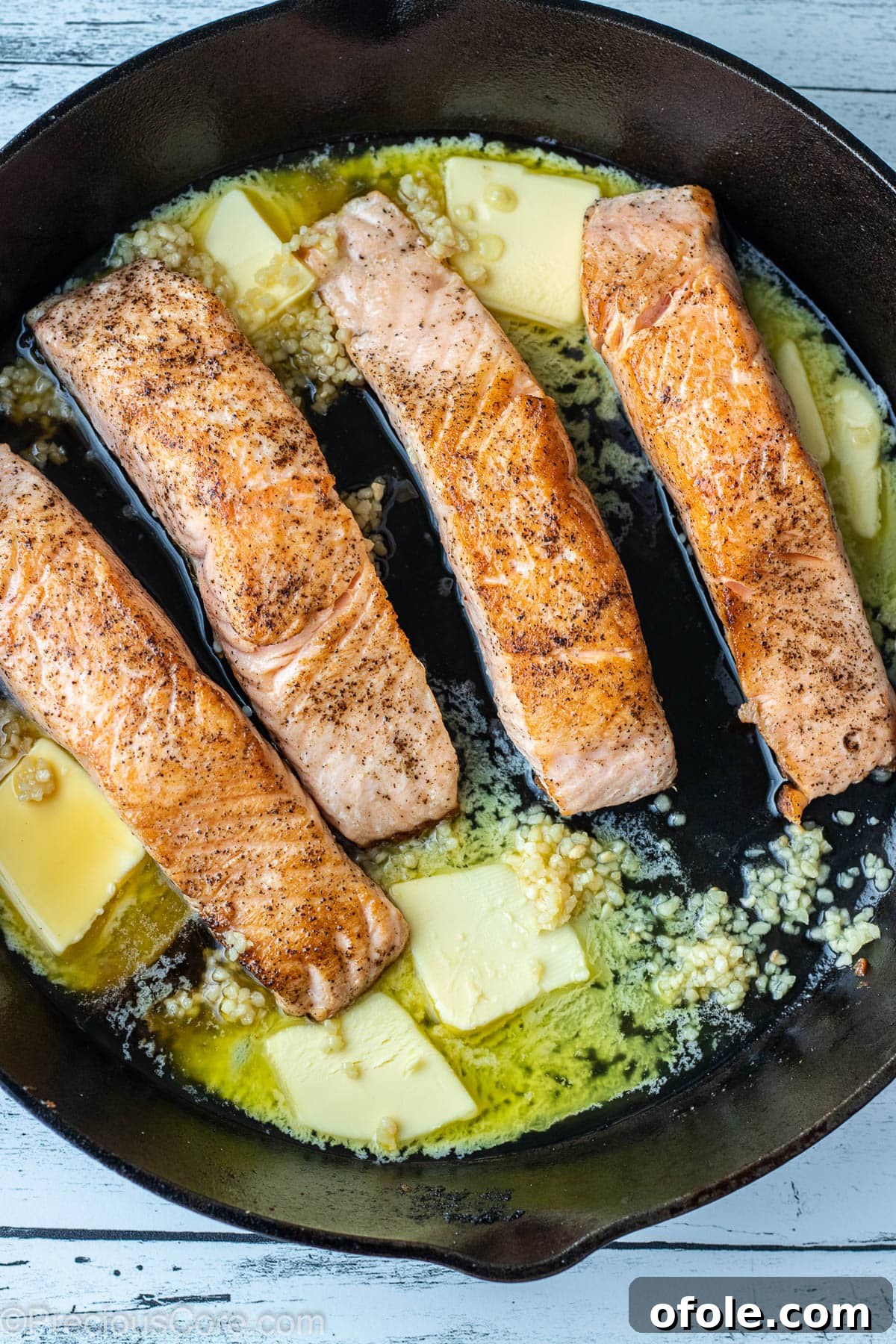 Melted butter and minced garlic being added to a cast iron skillet with seared salmon fillets, creating the sauce.