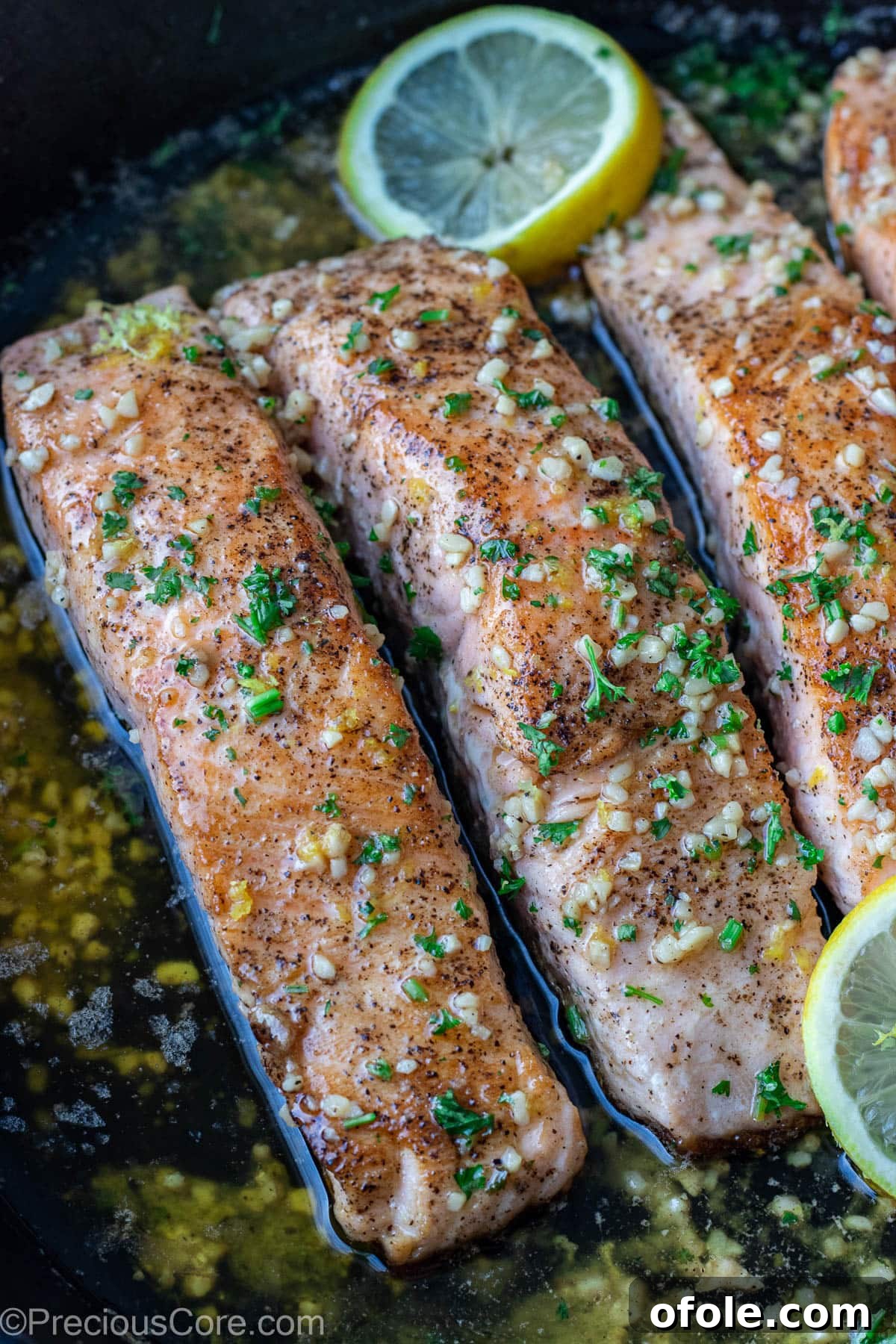 Finished lemon butter salmon in a pan, garnished with fresh parsley and vibrant lemon slices, ready to serve.