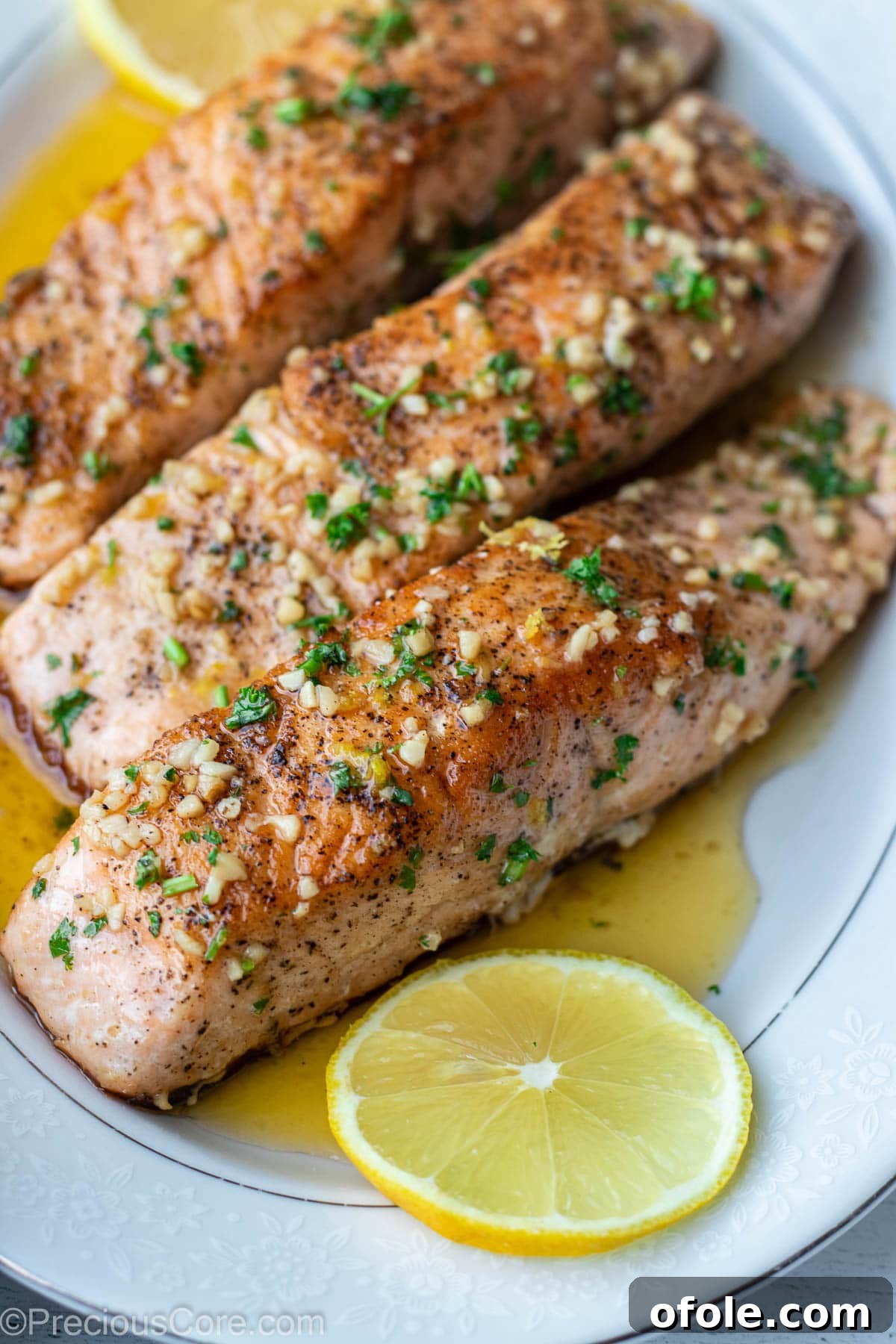 Three perfectly cooked salmon fillets on a serving tray, drizzled with lemon butter sauce and garnished with fresh herbs.