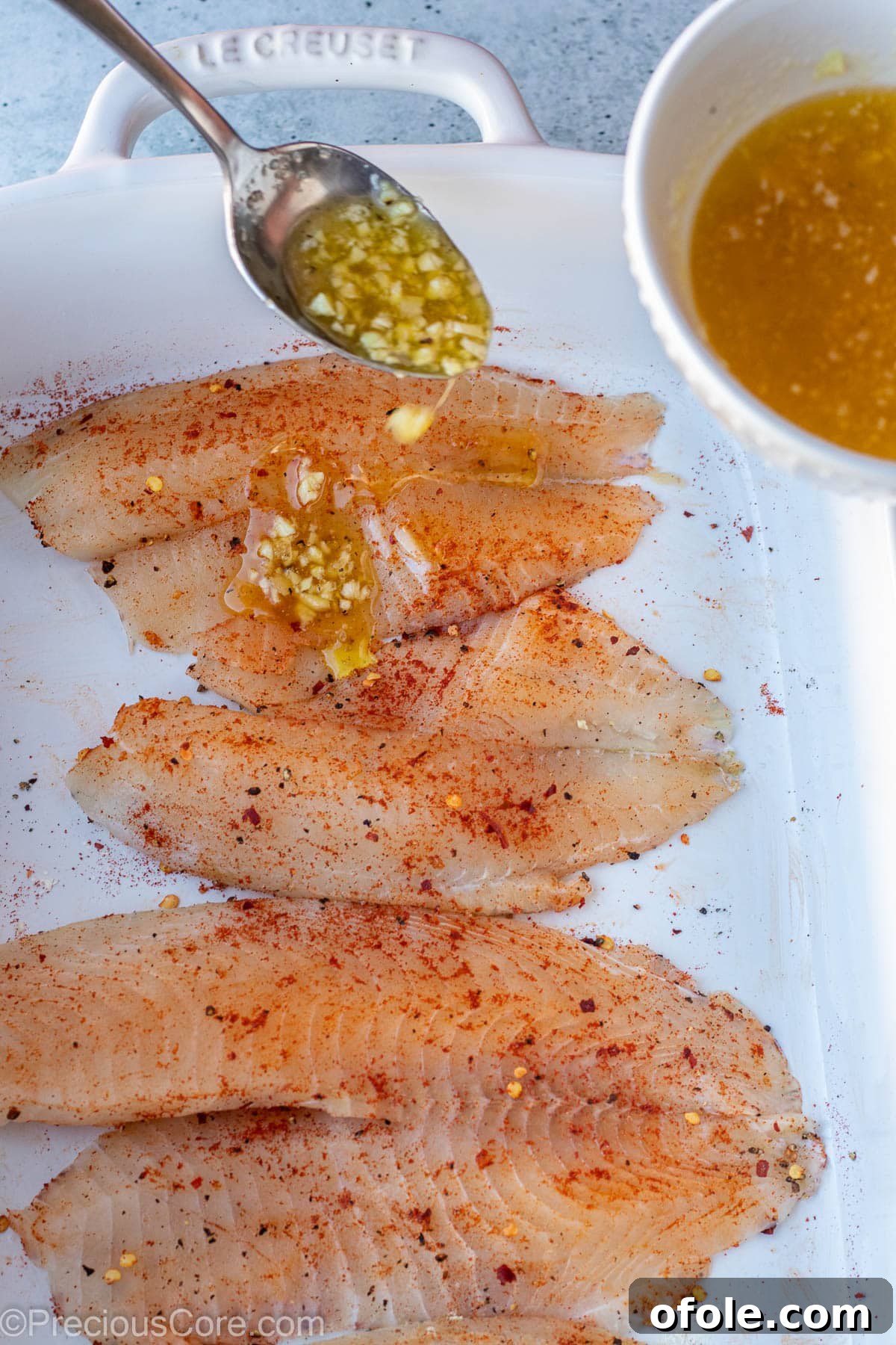 Garlic Butter Infused Tilapia 6 A spoon gracefully pouring rich garlic butter sauce over seasoned tilapia fillets.