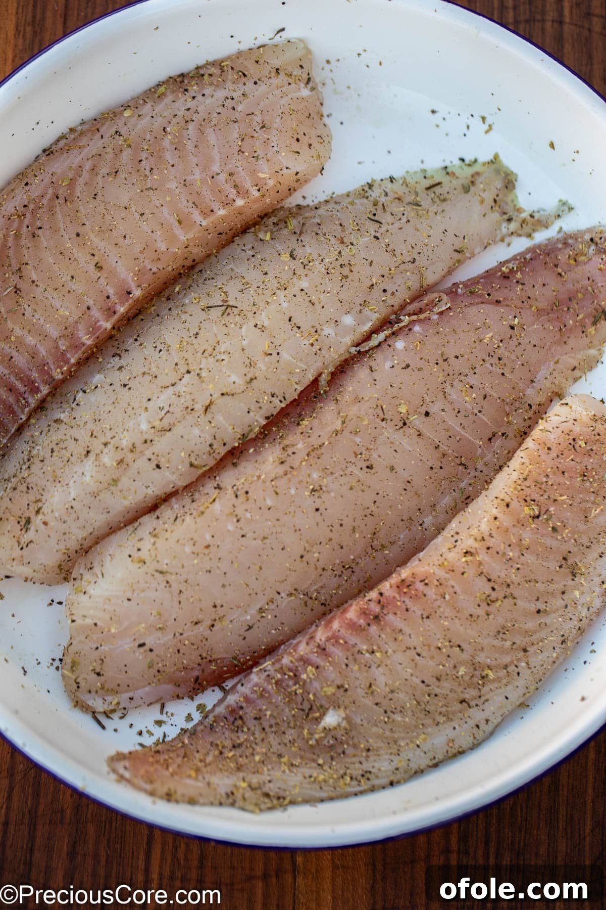 Velvety White Fish 5 Raw tilapia fillets carefully seasoned with salt, pepper, and Italian herbs, ready for cooking.