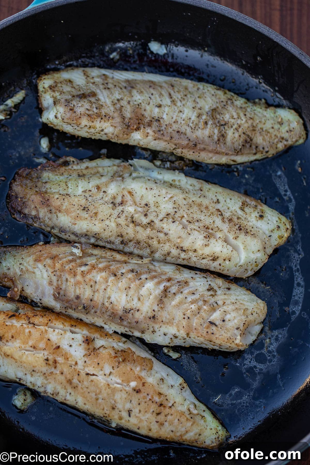 Velvety White Fish 6 Seasoned tilapia fillets searing in olive oil in a hot skillet, developing a golden-brown crust.