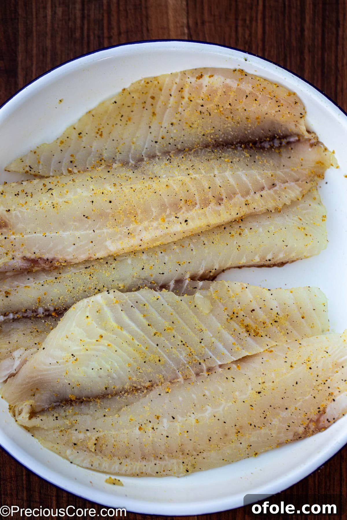 Seasoned tilapia fillets resting in a white ceramic bowl, ready for cooking.