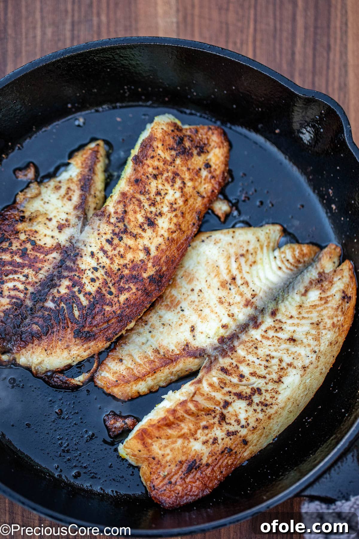 Two perfectly cooked fish fillets sizzling in a cast iron skillet, showcasing a golden crust.