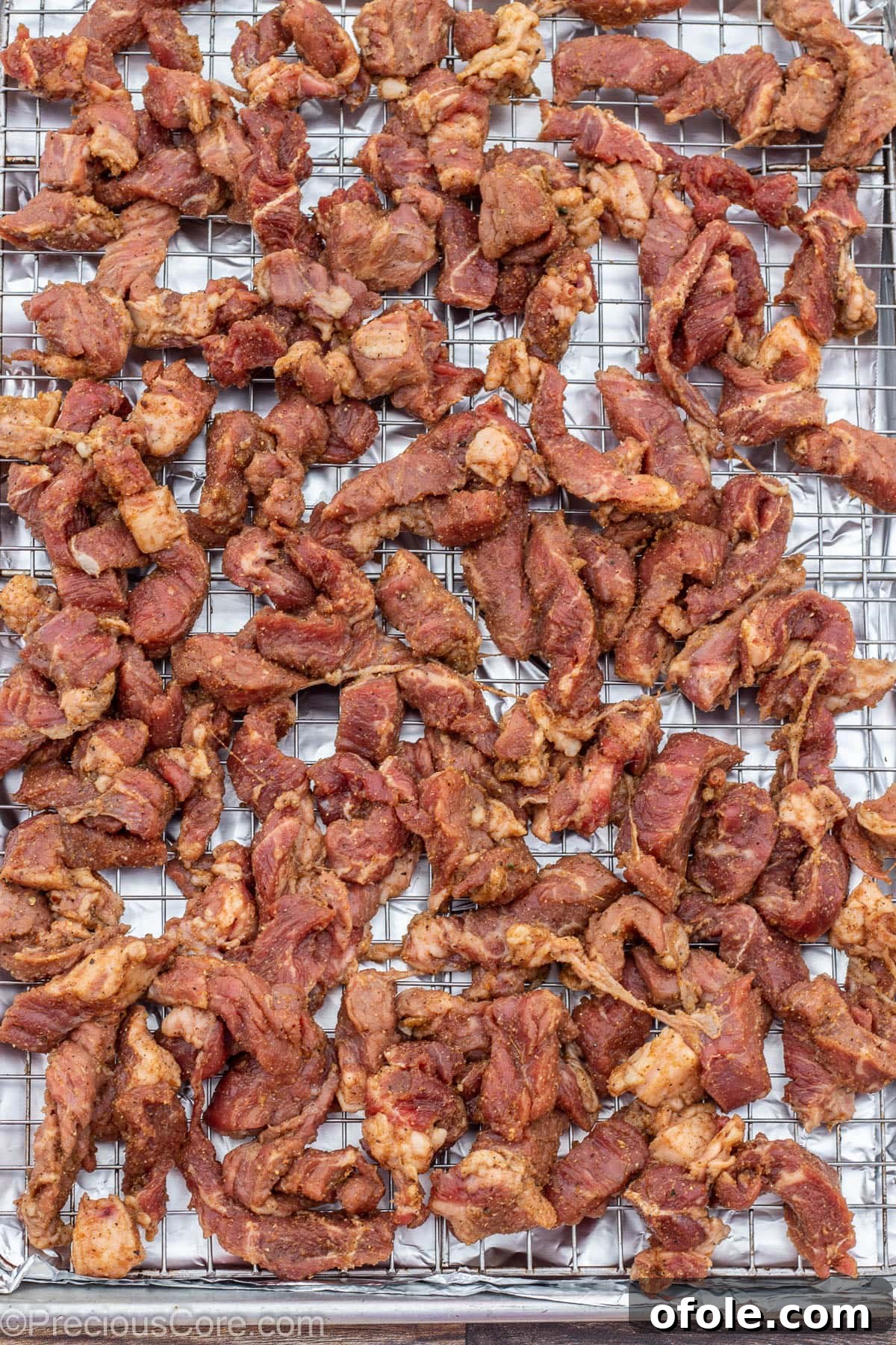 Cameroonian Soya Snack 7 Seasoned beef slices meticulously arranged in a single layer on a baking sheet with a wire rack, ready for broiling.