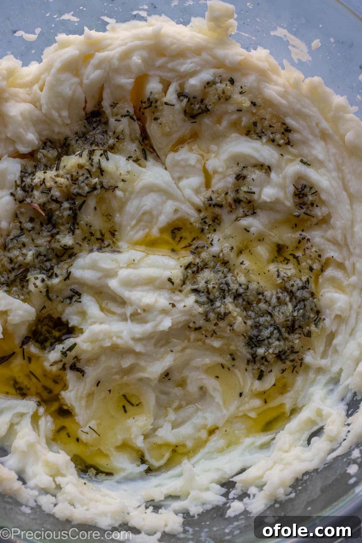 Aromatic Rosemary Garlic Mash 7 Melted butter and minced garlic and rosemary over mashed potatoes in a bowl.