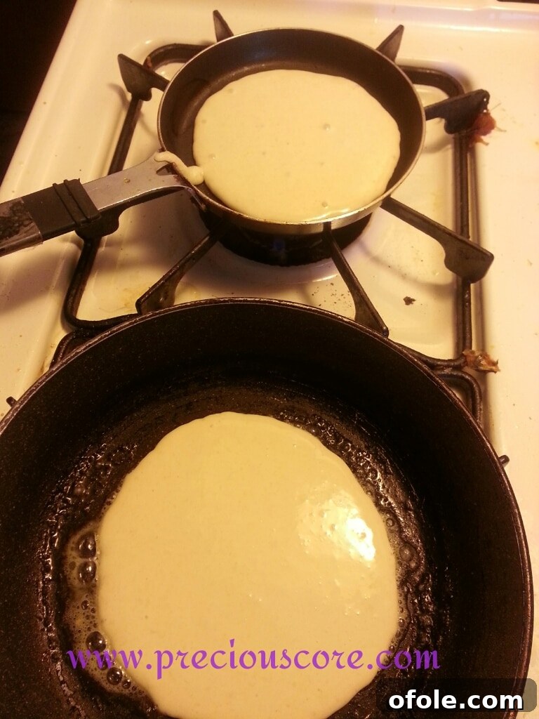 Several scoops of coconut pancake batter sizzling on a hot skillet with melted coconut oil.