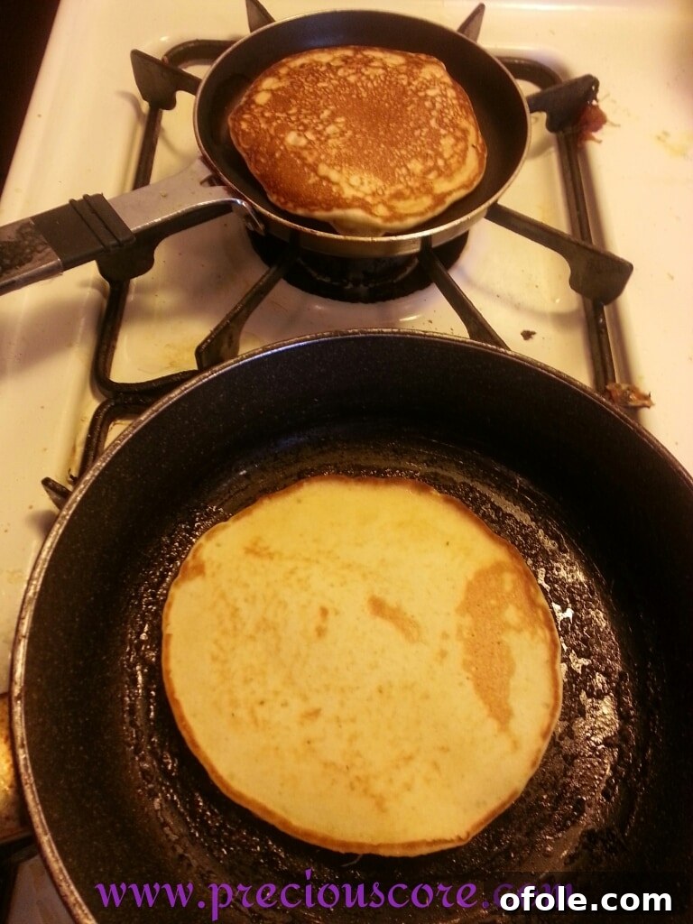 A fluffy coconut pancake being perfectly flipped in a skillet, revealing its golden brown cooked side.