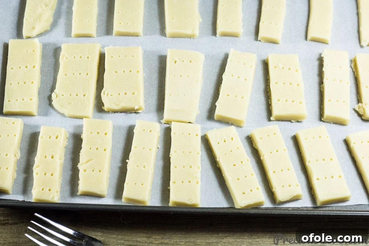Perfect Buttery Shortbread From Scratch 14 Shortbread cookies neatly arranged on a parchment-lined baking sheet, each pricked with a fork, ready for the oven.
