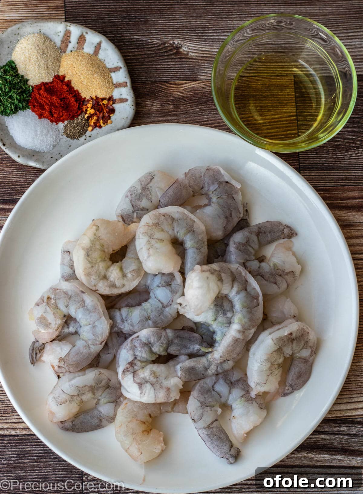 Sizzling Garlic Shrimp 3 Raw shrimp on a plate, a bowl of dried seasoning, and a small bowl of olive oil, ready for preparation.