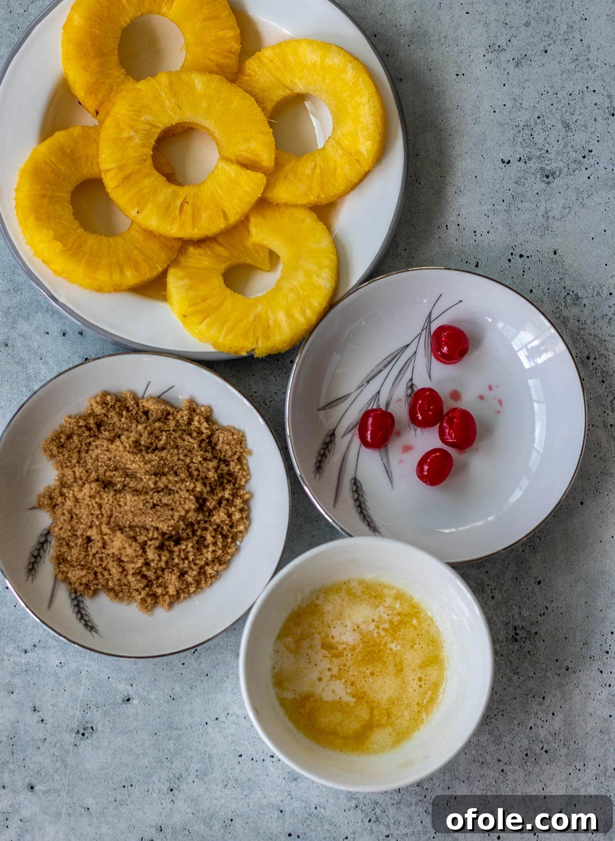 Pineapple rings, bright red maraschino cherries, brown sugar, and melted butter, ready for the bottom of the pan.
