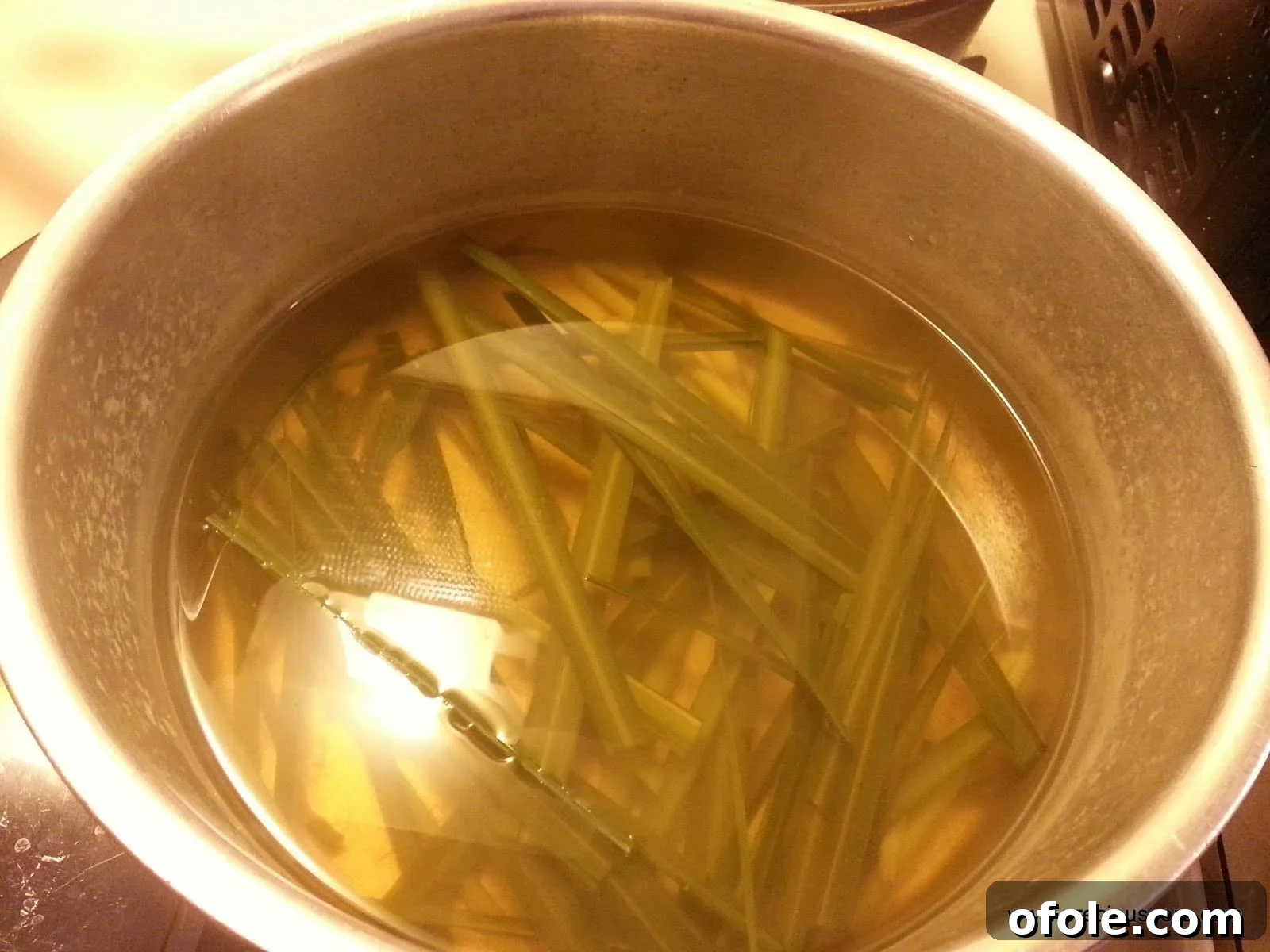 Hands preparing fresh lemongrass stalks for tea, showing the cutting process.