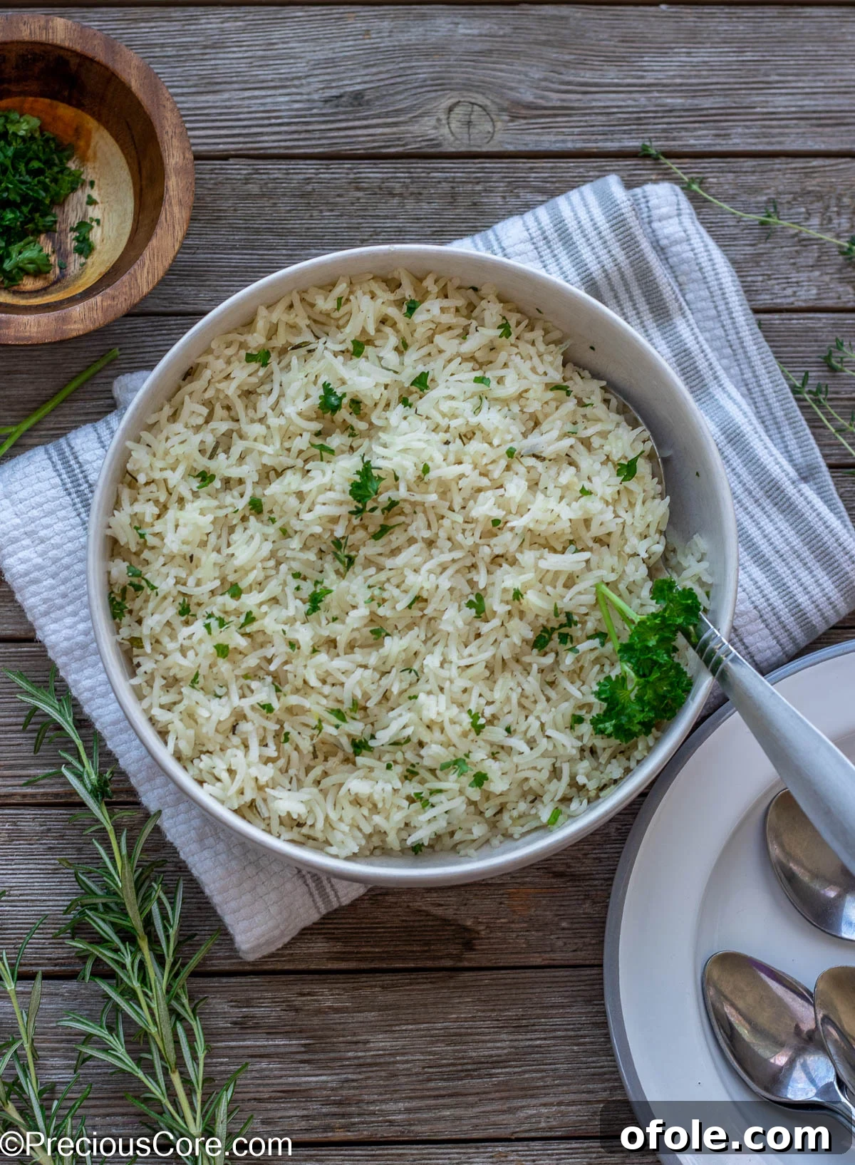 A bowl of perfectly seasoned garlic herb rice, garnished with fresh parsley, with dinner plates arranged elegantly beside it.