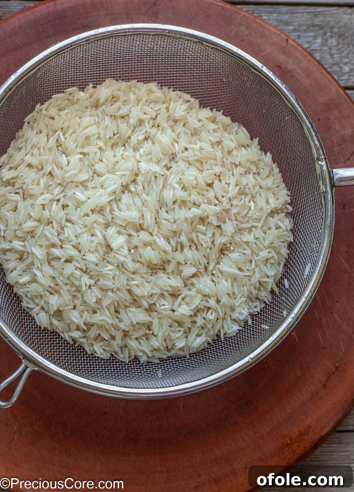 Freshly rinsed basmati rice resting in a fine mesh strainer, with clear water draining away from the grains.
