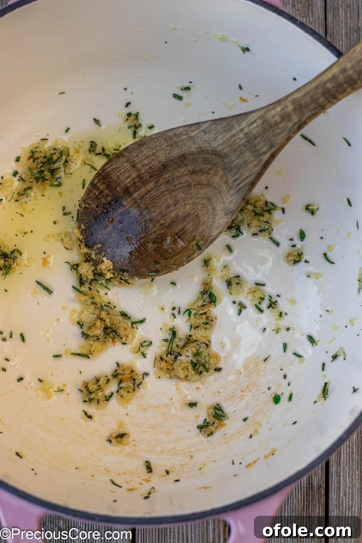 Minced garlic and fresh herbs, including rosemary and thyme, gently sizzling in olive oil within a cast iron enamel pot, releasing their fragrant aromas.
