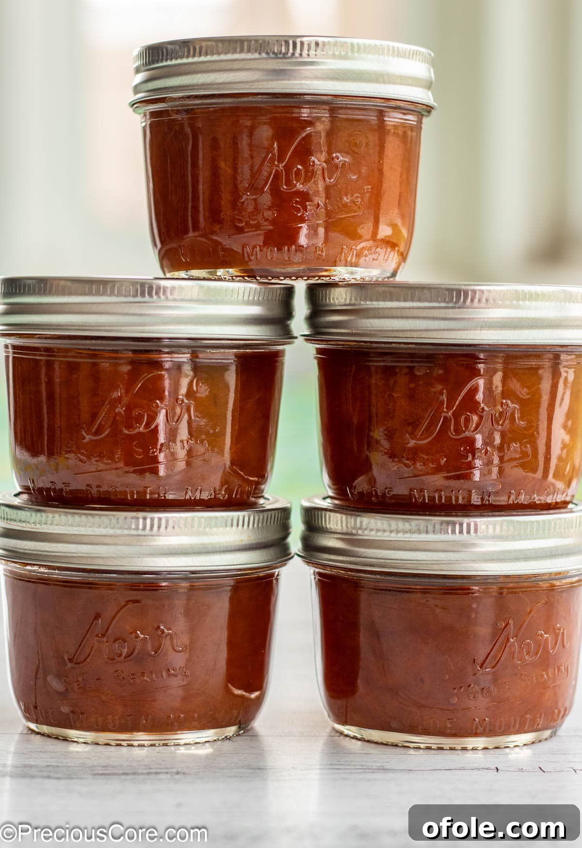 A stack of five sealed mason jars filled with homemade apricot preserves, showcasing successful canning and readiness for storage.