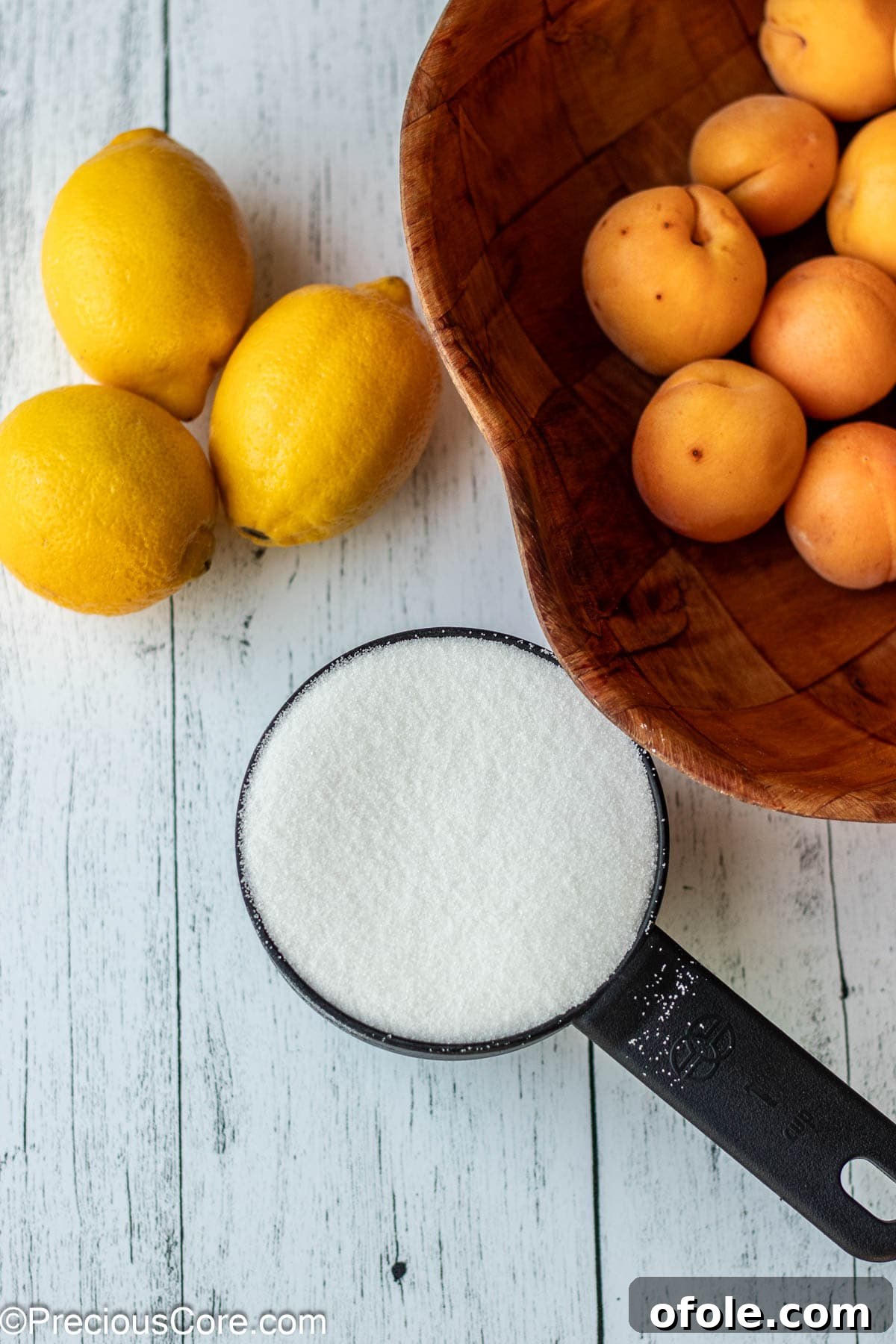 Fresh apricots, a whole lemon, and granulated sugar laid out on a wooden cutting board, highlighting the simple ingredients needed for the preserves.