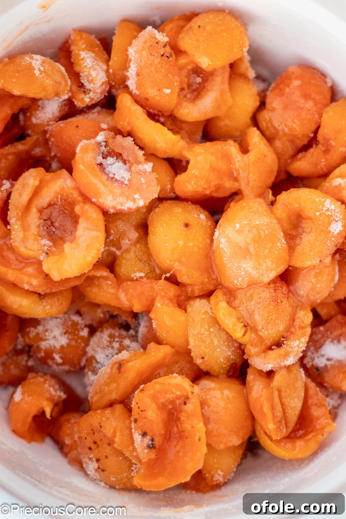 Halved apricots, glistening with granulated sugar, mixed in a white ceramic bowl, ready for the next step of preserve making.
