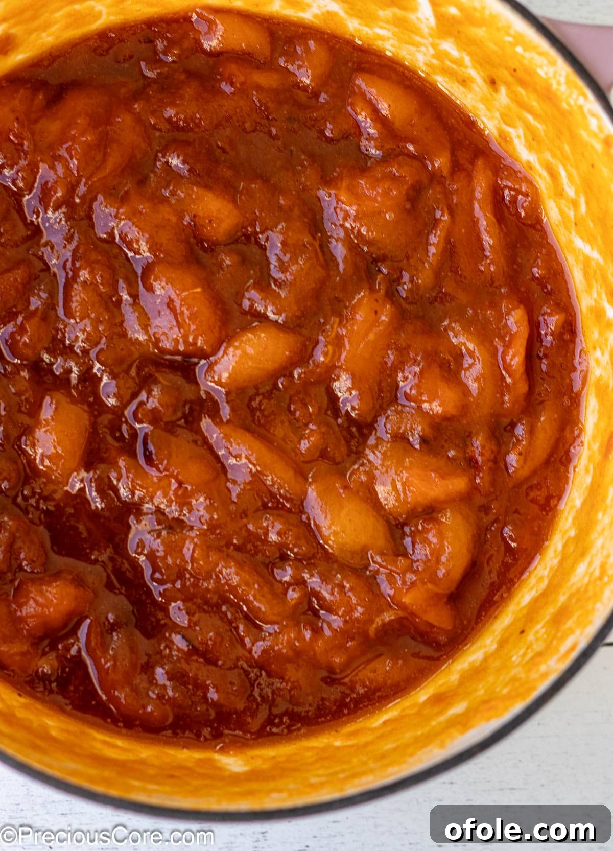 Apricot preserves simmering in an enameled cast iron pot, their vibrant color intensifying with cooking.