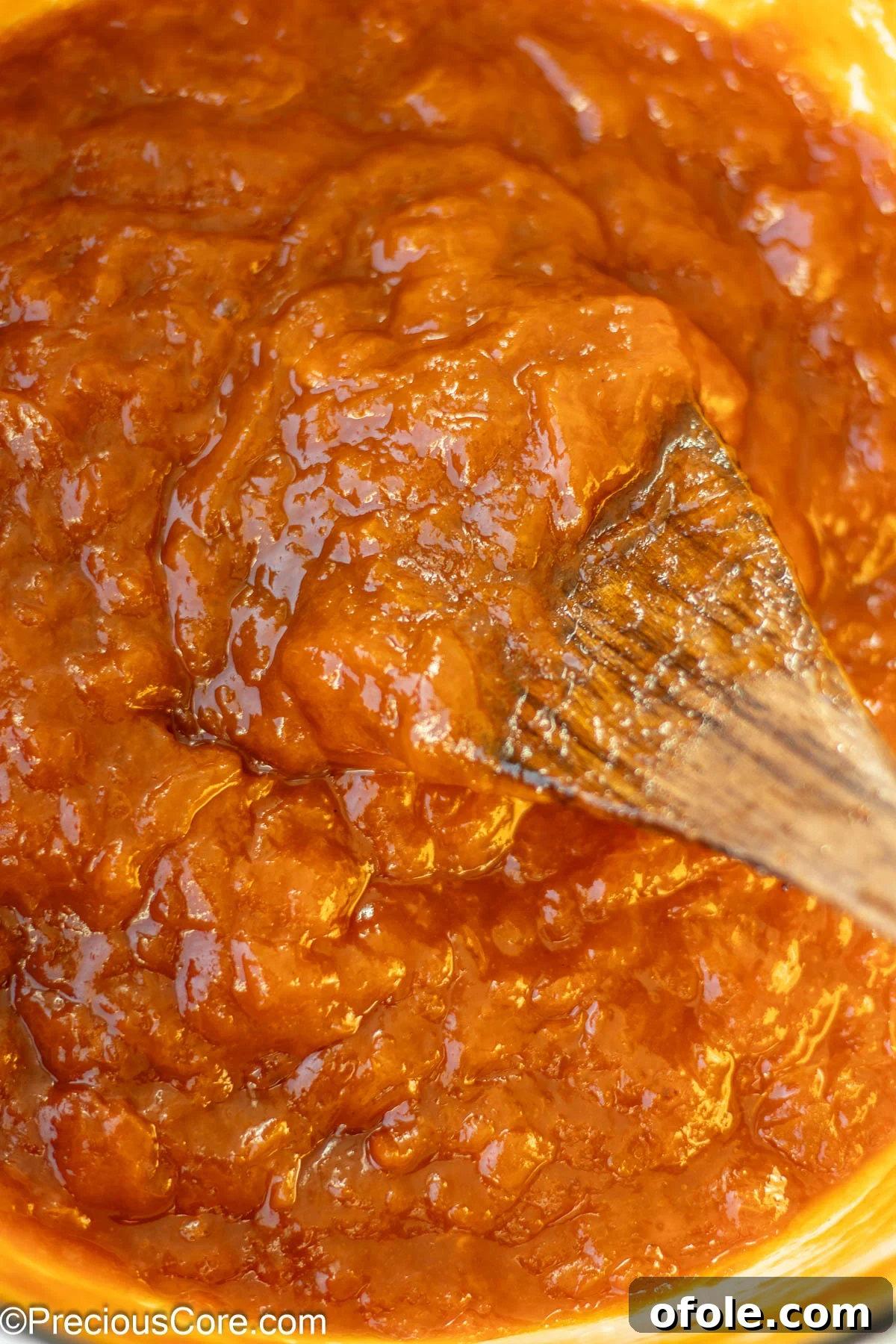 Fully cooked apricot preserves in a pot with a wooden spoon resting in it, showcasing the perfect thick, jammy consistency.