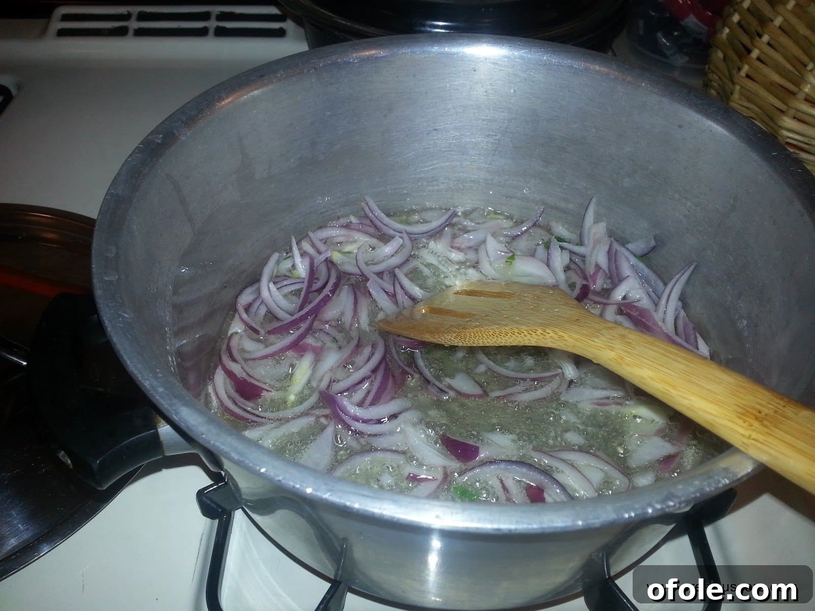 Finely chopped onions gently sautéing in hot vegetable oil in a pot, creating an aromatic and sweet base for the dish.