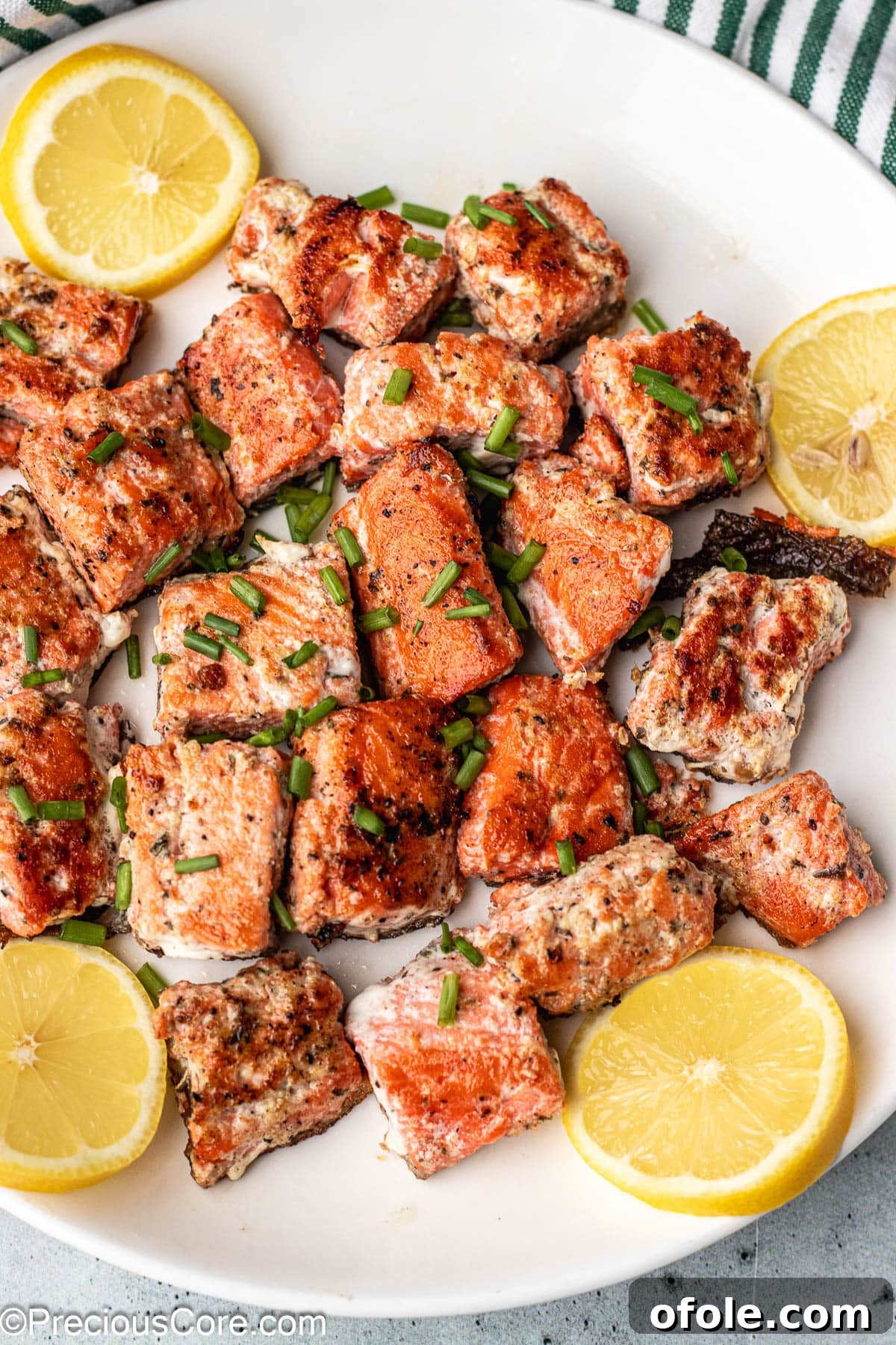 Irresistible Salmon Bites 8 Perfectly cooked salmon bites on a white plate, garnished with fresh lemon slices and dill.