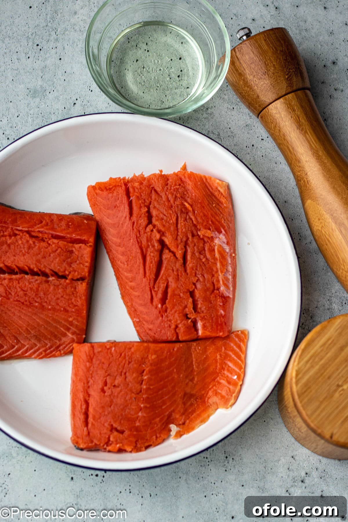 Fresh sockeye salmon fillets, a bottle of olive oil, and a small bowl of salt and pepper.
