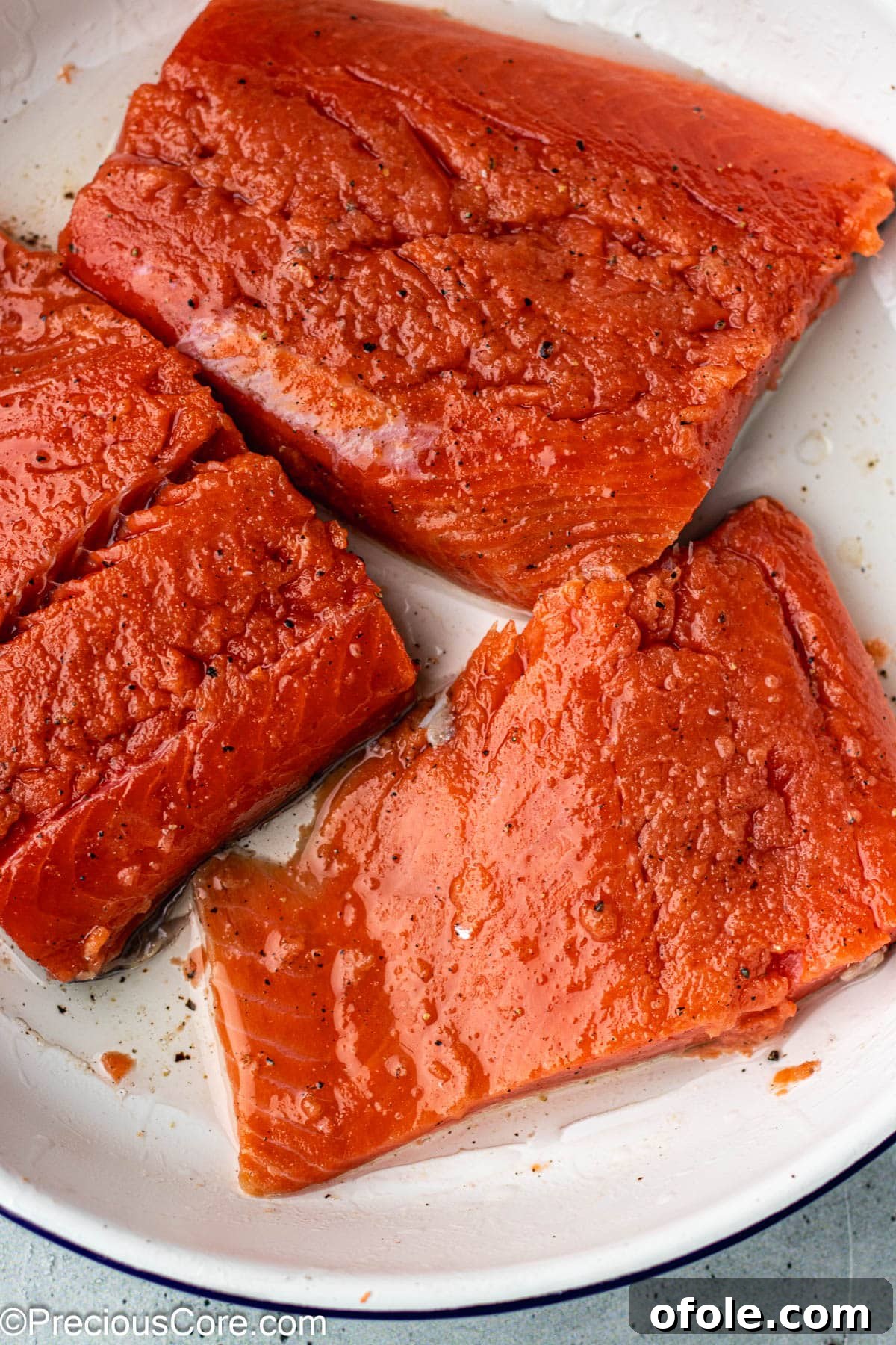 Sockeye salmon fillets generously seasoned with olive oil, salt, and pepper in a white bowl.