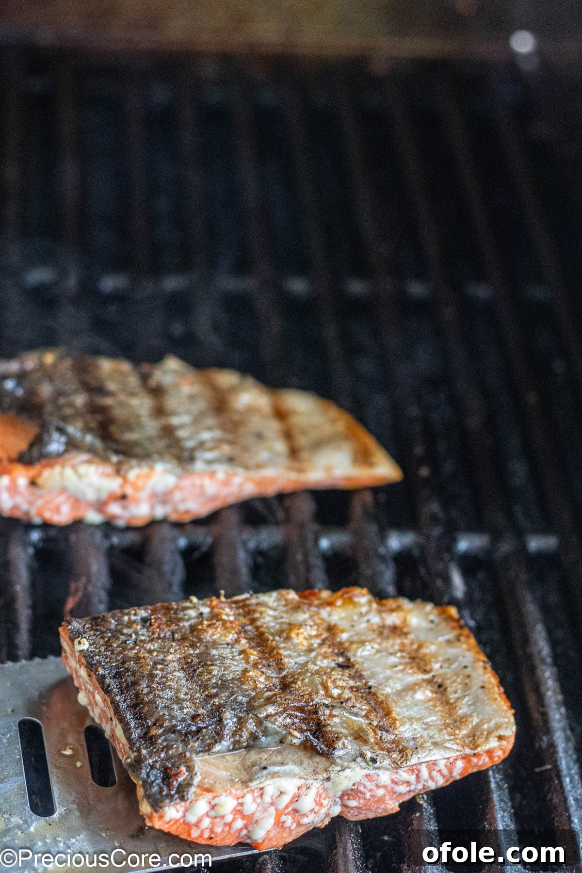 Skin-on sockeye salmon fillets cooking on a hot grill, showing distinct grill marks.