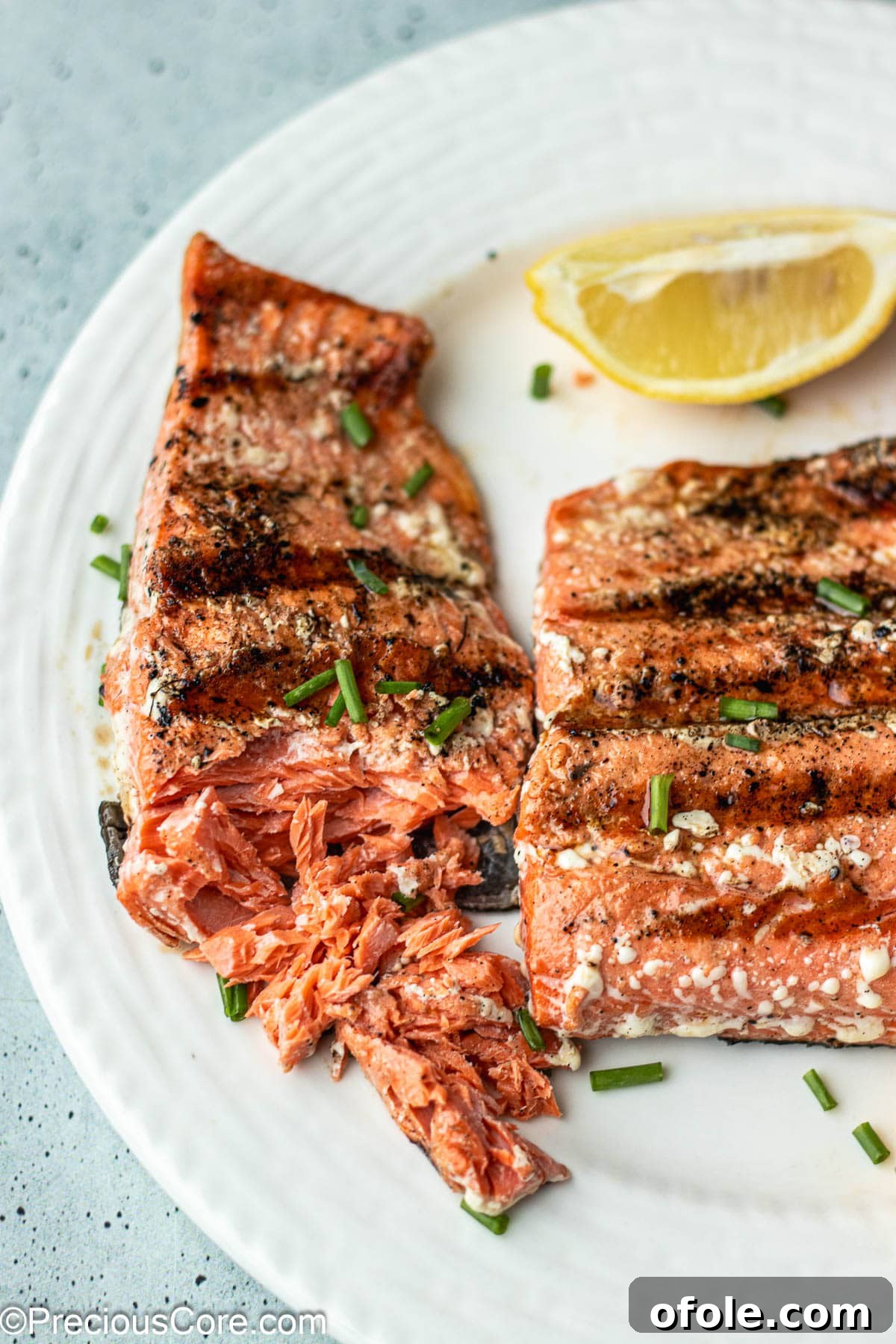 Two grilled salmon fillets on a plate, one partially flaked with a fork to show doneness.