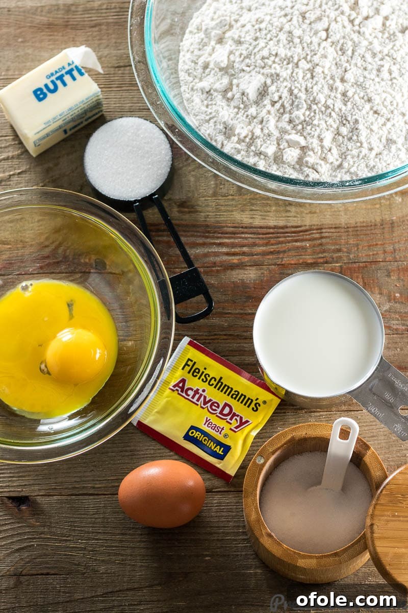 A selection of ingredients for sweet dinner rolls laid out on a table, including flour, butter, milk, sugar, yeast, salt, and eggs.
