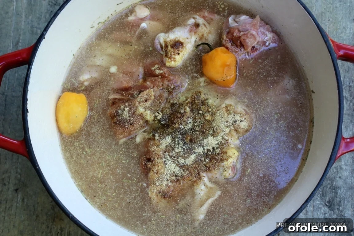 Raw chicken and blended spices simmering in a pot, showing the early stages of pepper soup