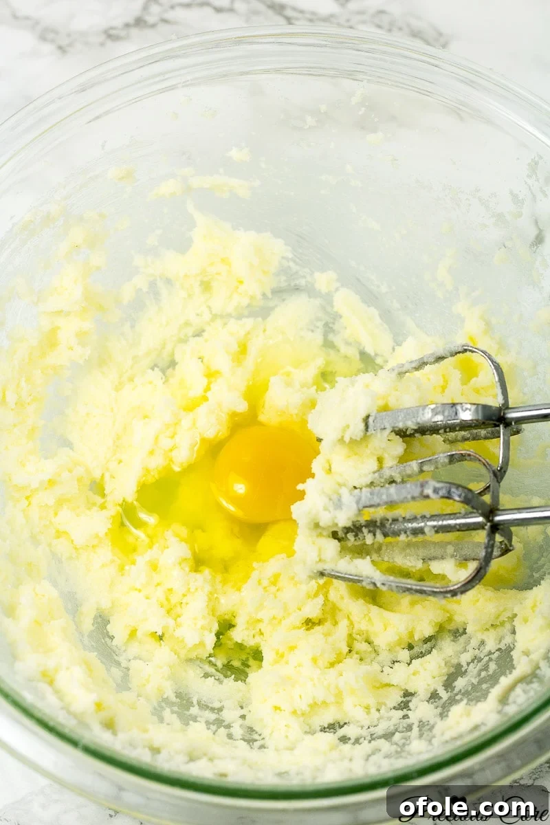 Timeless Fresh Apple Cake 8 Eggs being added one by one to the creamed butter and sugar mixture in a mixing bowl.