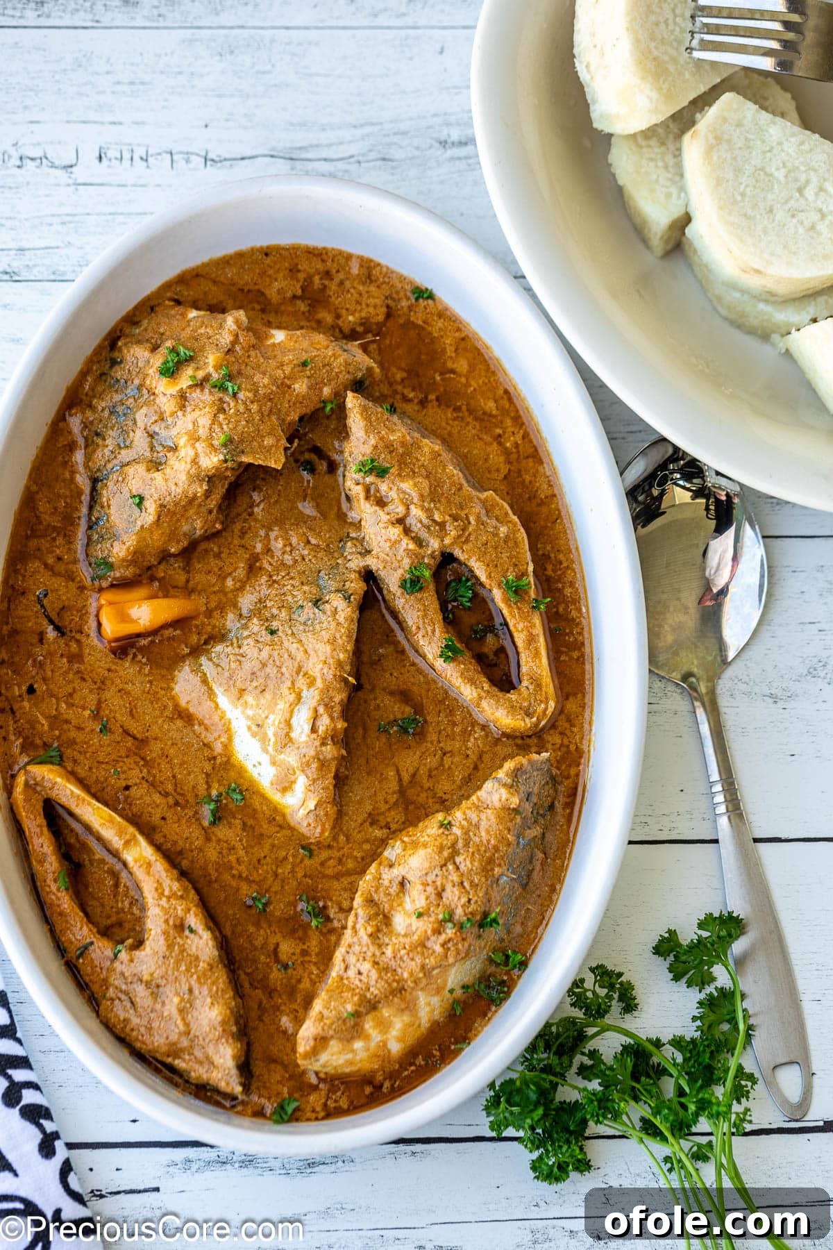 Njangsa sauce in a white oval bowl with white yams on the side, highlighting its creamy texture.