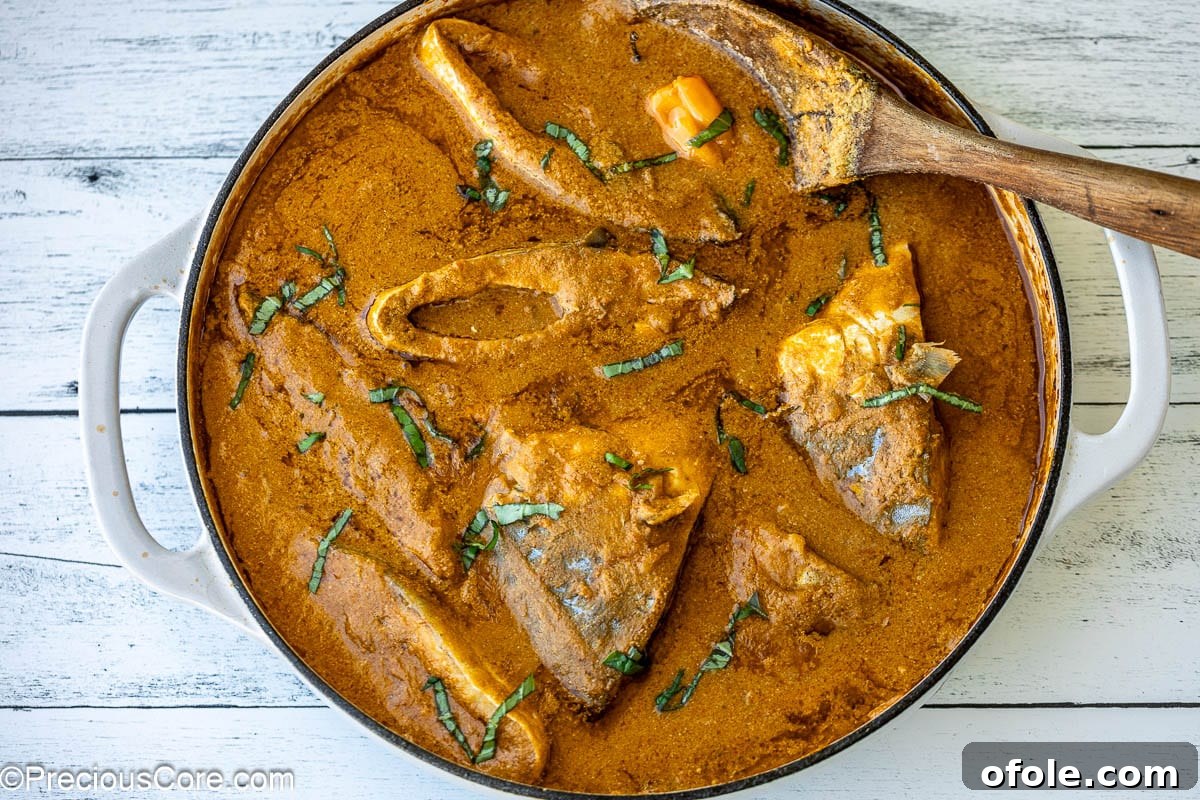 A white pot filled with rich, creamy Njangsa stew and firm fish steaks.